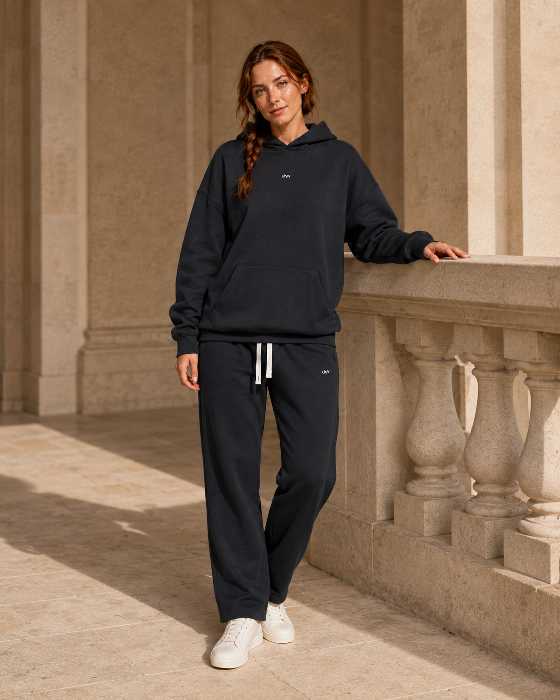Adult woman wearing the Black ULYV matching hoodie and sweatpants, full length editorial view