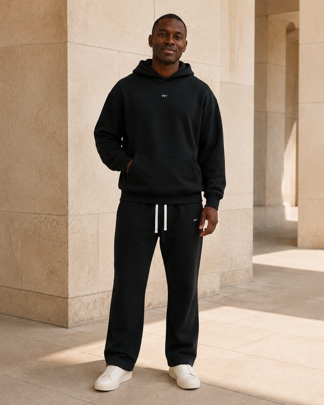 Adult model in the ULYV Black matching hoodie and sweatpants, full length view
